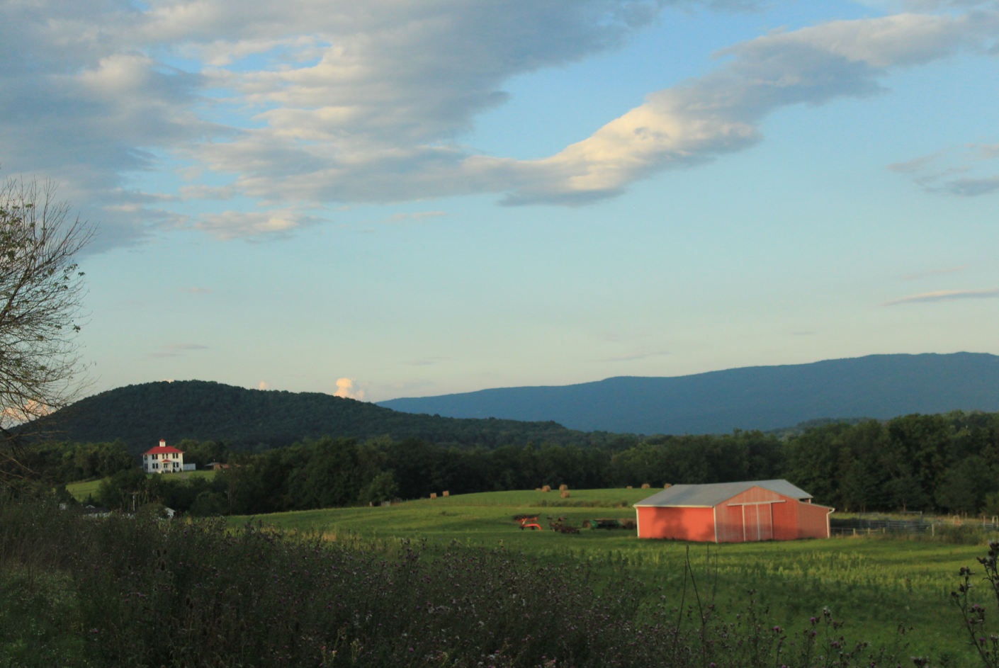 A working farm, a barn, and a white house with a red roof against a mountain ridge