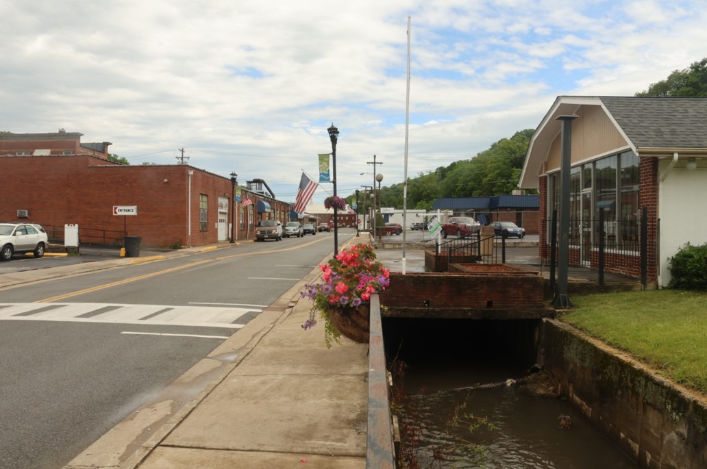 A Bluefield sidewalk and storefronts beside an open creek channel.